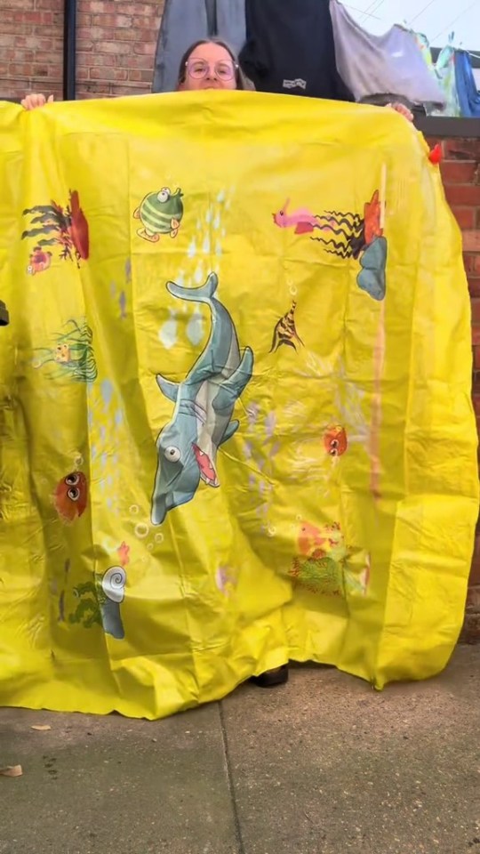 Person holding up a large yellow splash pad with underwater-themed illustrations.