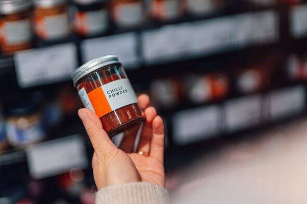 Close-up of young woman doing grocery shopping in supermarket, holding a jar of chilli powder