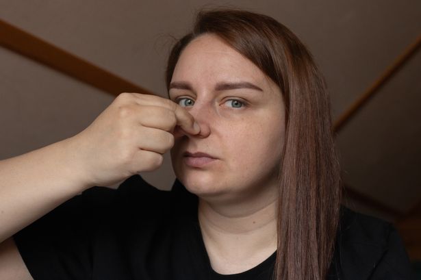 A woman indoors with long hair, pinching her nose due to an unpleasant odor.