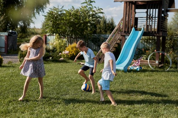 Three children playing soccer in garden