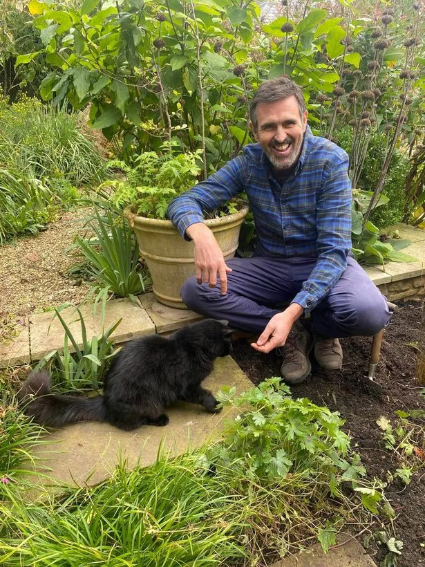 Adam Frost in his garden at home with Ash the cat