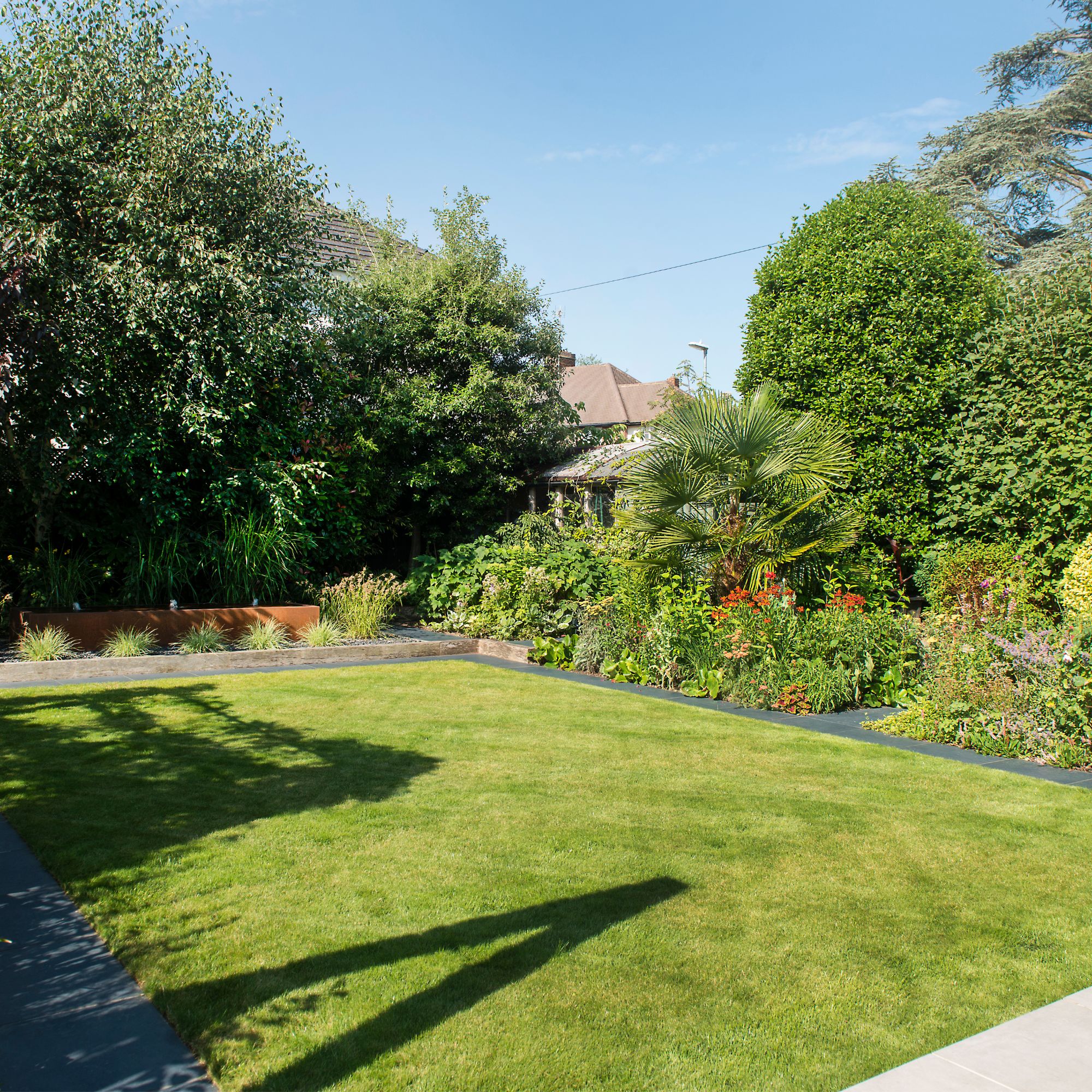 Cut grass lawn in garden surrounded by border plants and trees