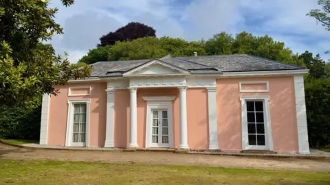 Plymouth City Council A house painted a salmon pink colour with white accents. The roof is grey.