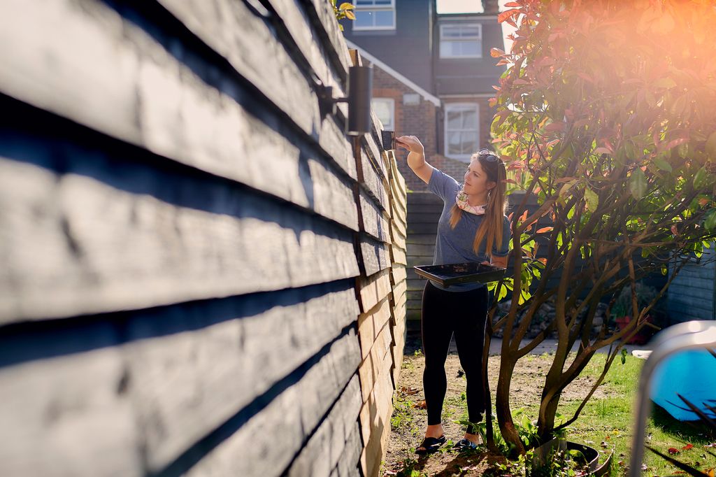 full length creative angle of woman painting black fence with brush