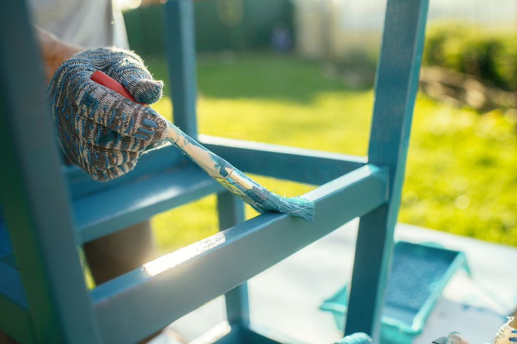 Senior man renovating a chair outdoors at back yard in sunny evening. Old furniture renovation. Sustainability concept.