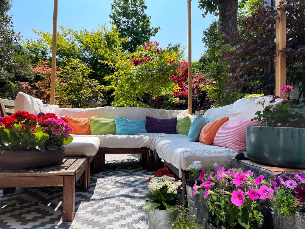 Stock photo showing ornamental Japanese-style garden with outdoor lounge area in Summer. Featuring a large expanse of white, interconnecting, white plastic decking tiles with outdoor patterned rug, providing a family space for outdoor hardwood, cushion covered seating.