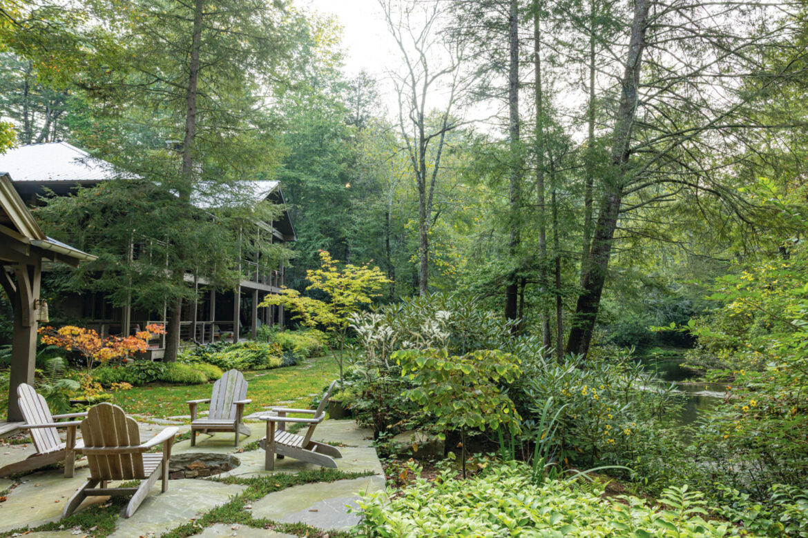 This Lush Mountain Hideout Near Cashiers Extends a Wet and Wild Welcome – Garden & Gun A garden at the back of a house in woodland. It has a firepit surrounded by chairs