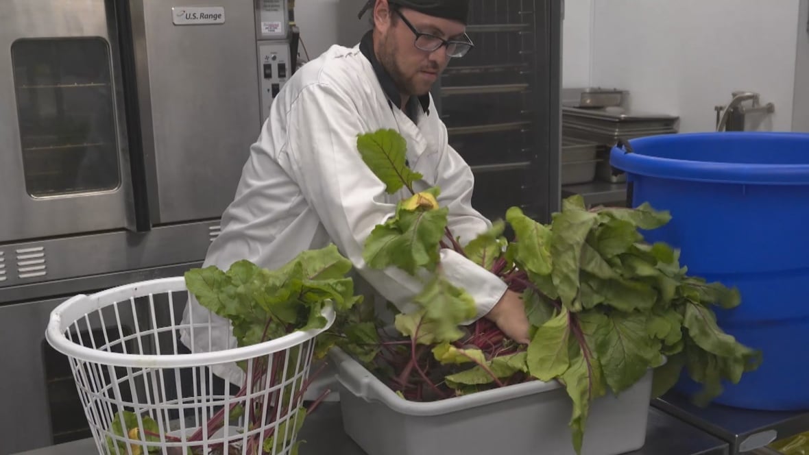 A man in a chef's uniform loads beets into a basket in a commercial kitchen.