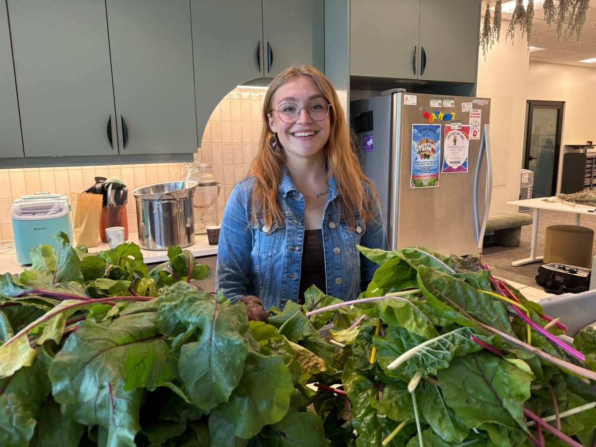 A smiling woman stands with fresh produce in a kitchen.
