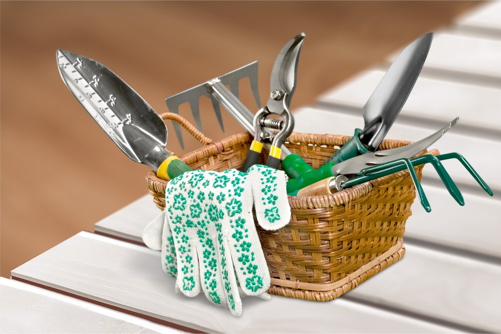 Gardening tools and gloves set in a brown wicker basket. Tools have green handles.
