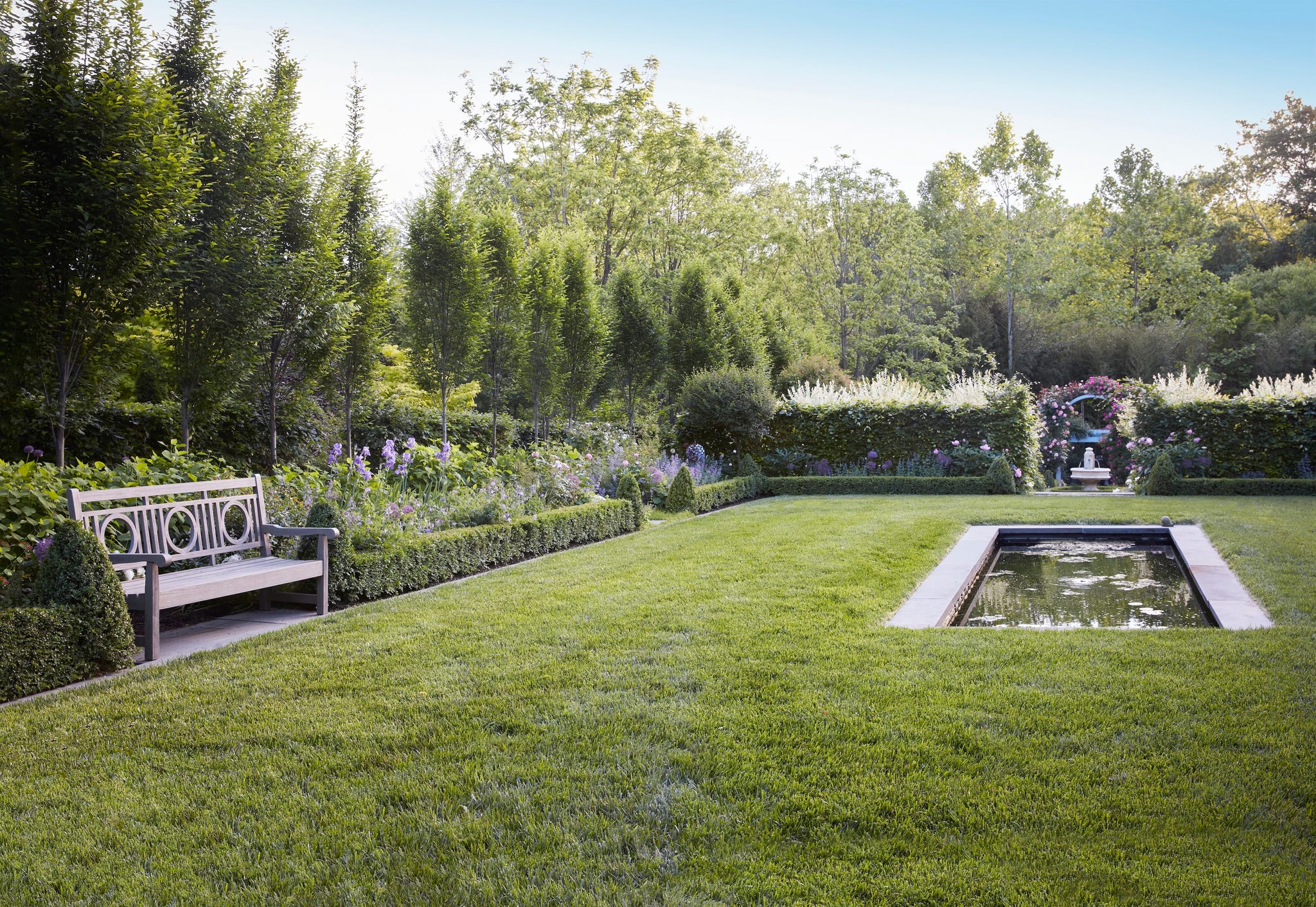 garden in the northern virginia home of master gardener, yvonne tsikata. a teak bench (restoration hardware) nestled among boxwood hedges is an inviting perch for pausing beside a reflecting pool inspired by england’s 16th century wollerton old hall garden.