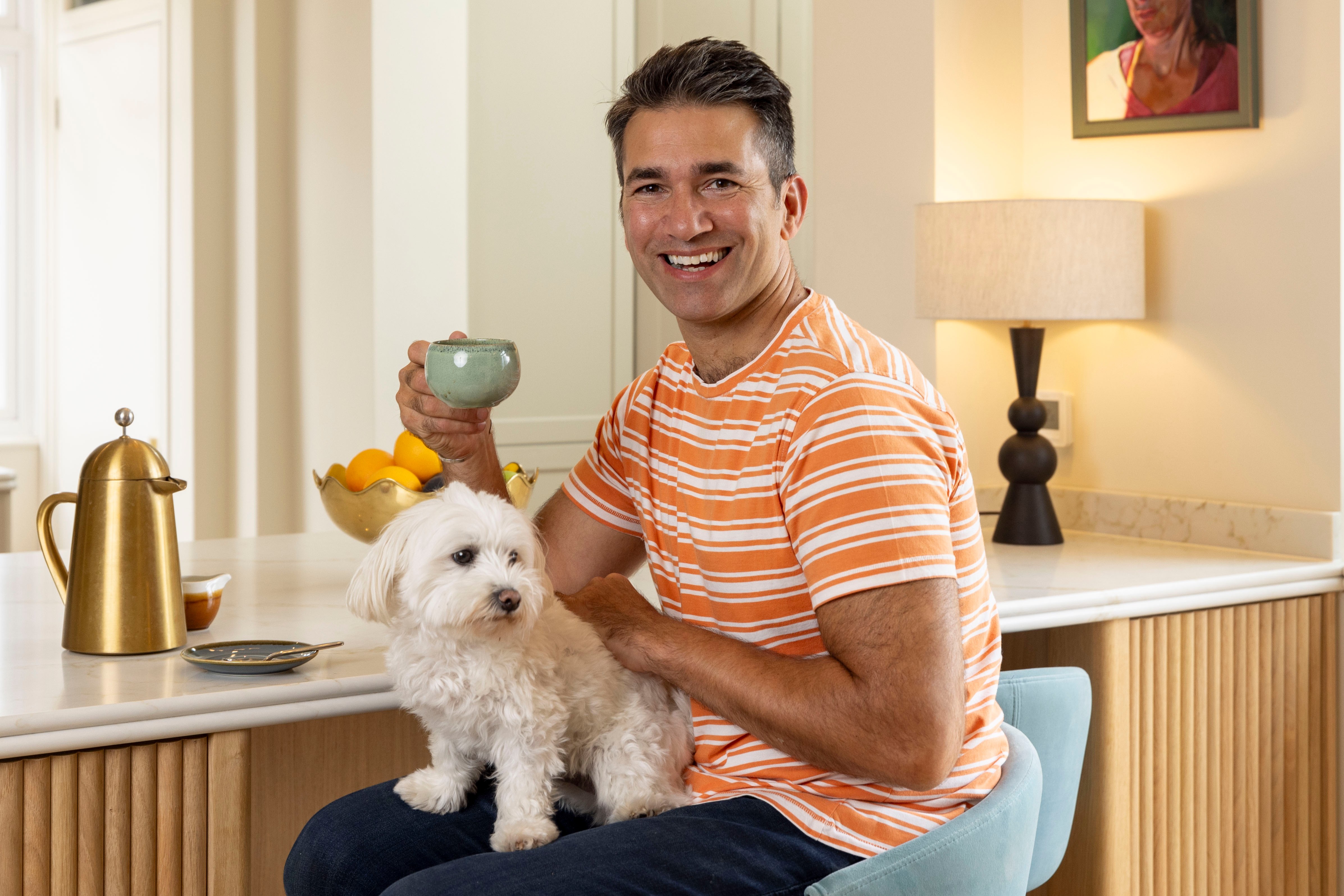 A man sits at his kitchen island with his dog, holding a cup.