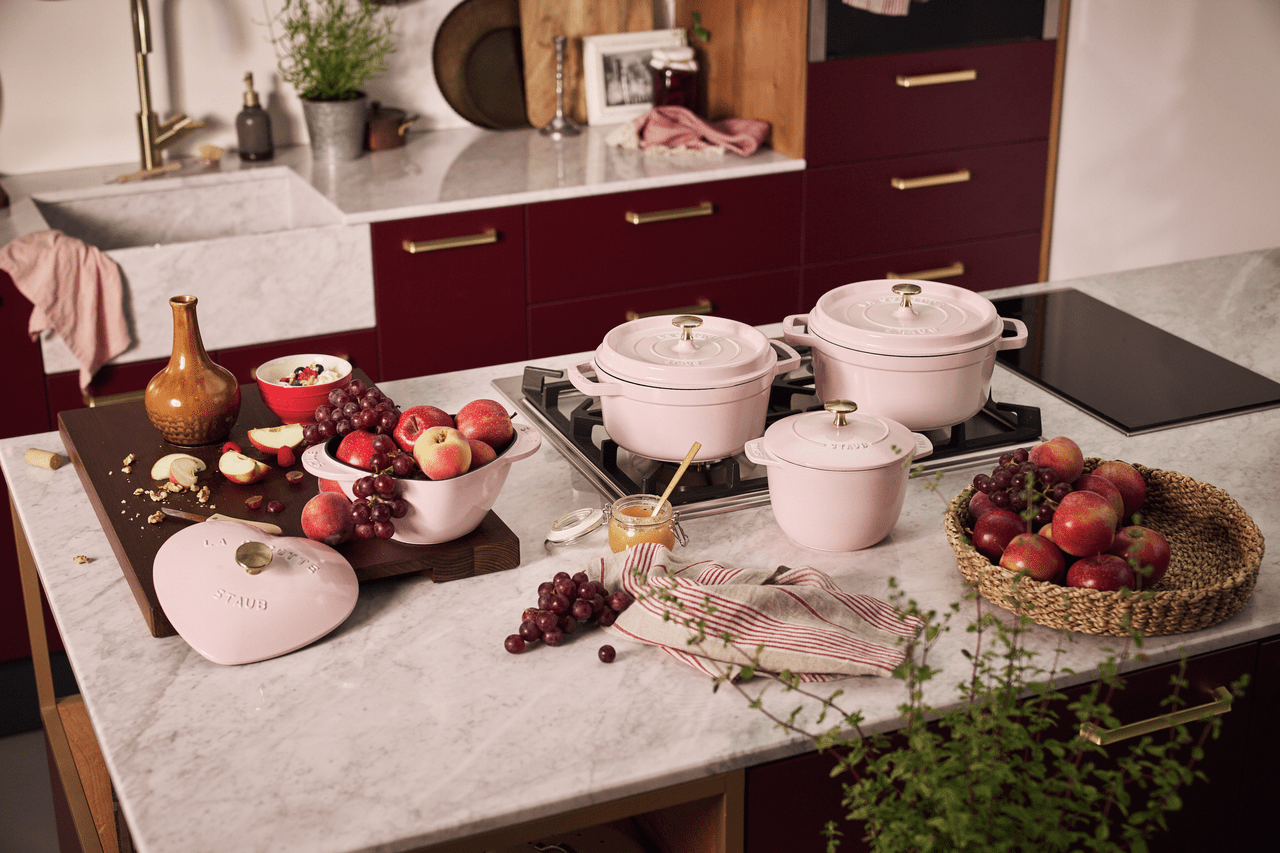 Pink Staub cookware on a kitchen counter with fruit.