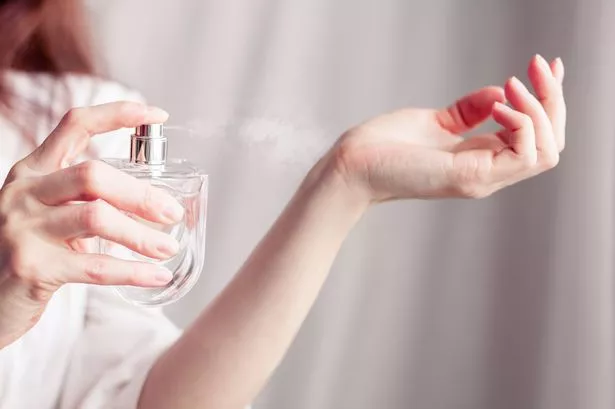 Close up of a person spraying a bottle of perfume onto their wrist