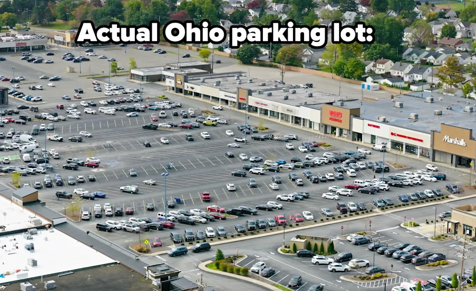 Aerial view of a busy parking lot outside a shopping center with various stores, surrounded by residential neighborhoods and trees