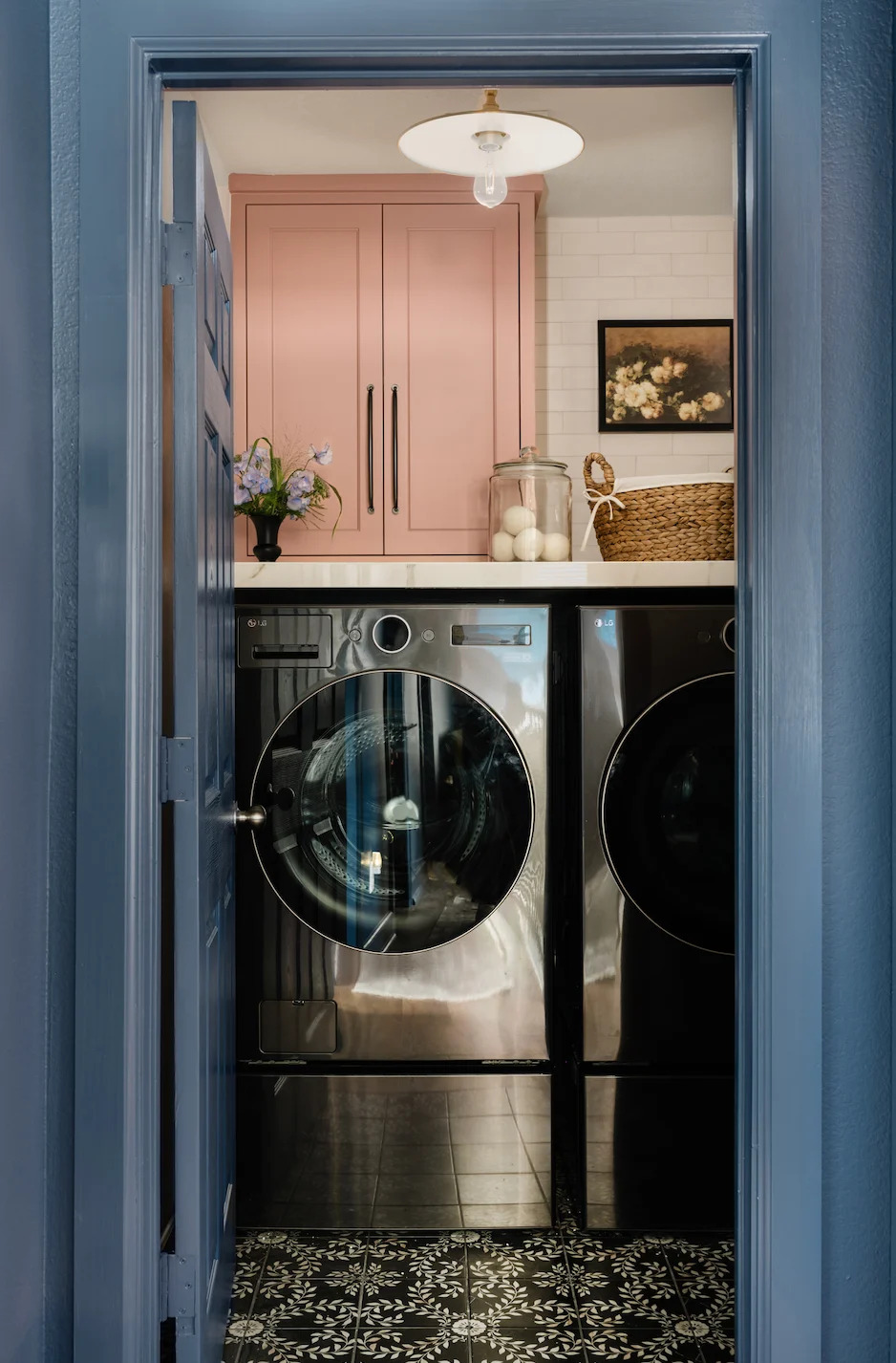 a laundry room with a silver washing machine, a pink cupboard, blue doors, and black and white tiling