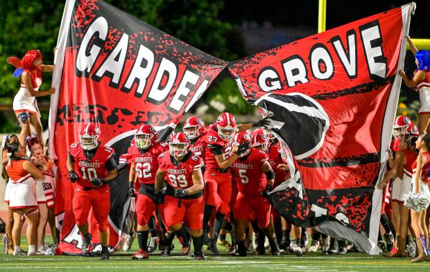The Garden Grove football team breaks through the banner as...