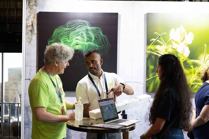 Group of three people standing around a laptop on a table with a man pointing to a plastic contraption in his hand