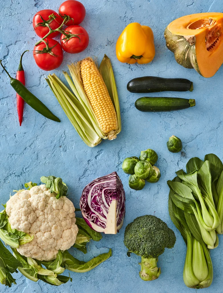 fruiting vegetables on blue background with tomato corn cabbage broccoli pumpkin and cauliflower