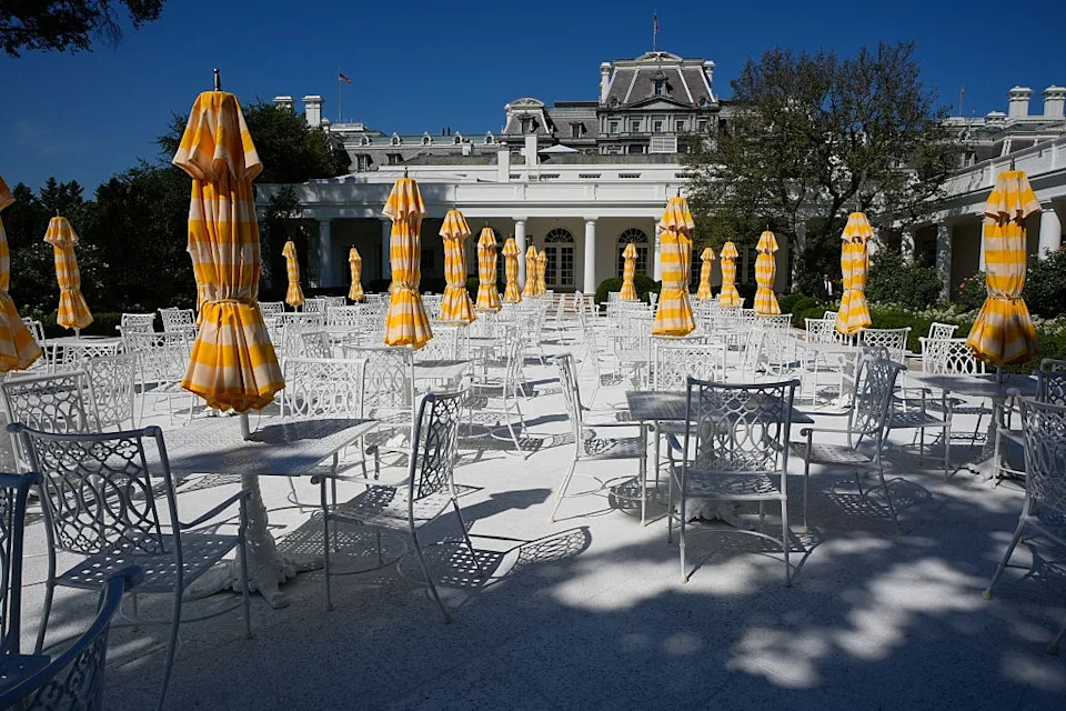 Outdoor cafe setting with white furniture and yellow-striped umbrellas, against a historic building's backdrop