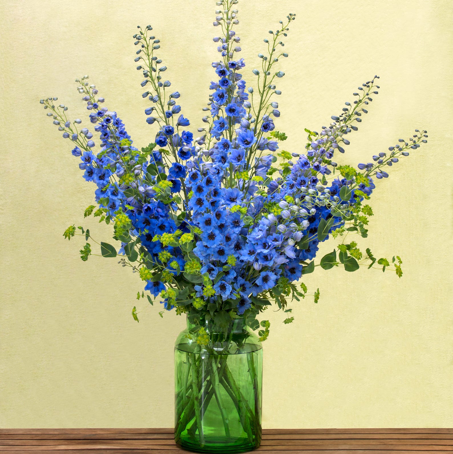 a blue delphinium arrangement in a green vase
