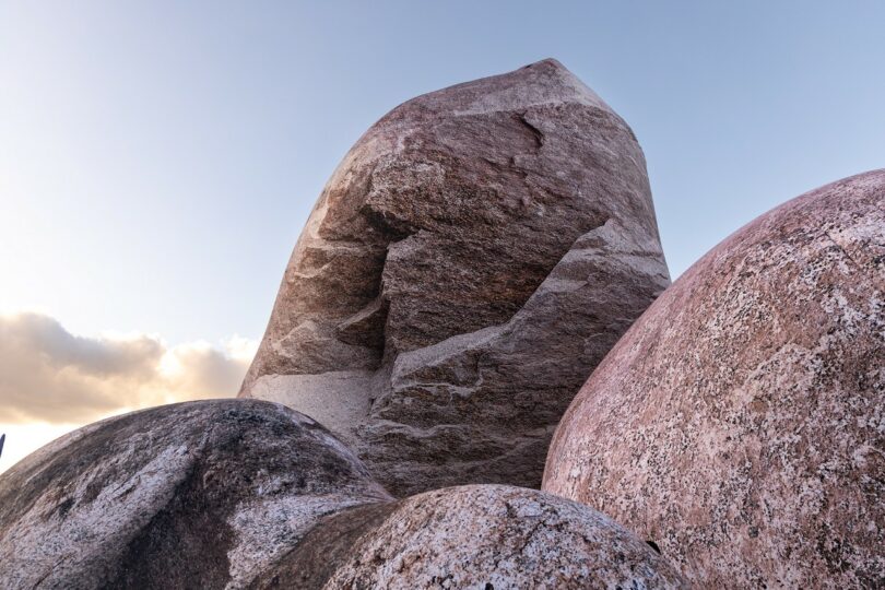 Large, smooth granite boulders with a prominent, upright rock formation against a clear sky at sunset