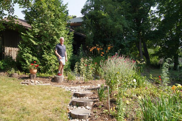 Robert Brown stands by his rain garden installed through the City of Peterborough's Rain Garden Subsidy Program. Robert's yard slopes toward the street, so by strategically placing his rain garden at the top of the yard, his garden catches and slowly releases water into the gardens below. (Photo: Yvonne Hollandy / GreenUP)