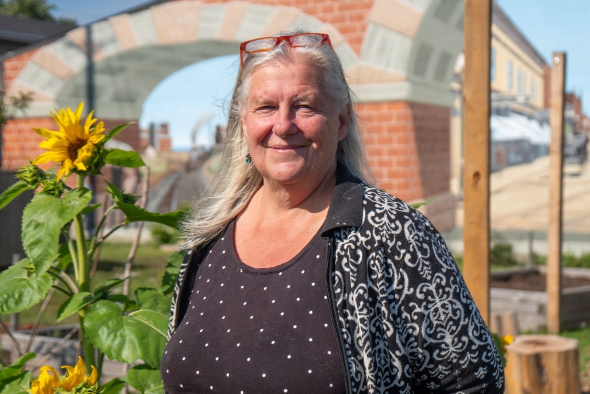 A person is seen standing in a garden. There are sunflowers beside them.