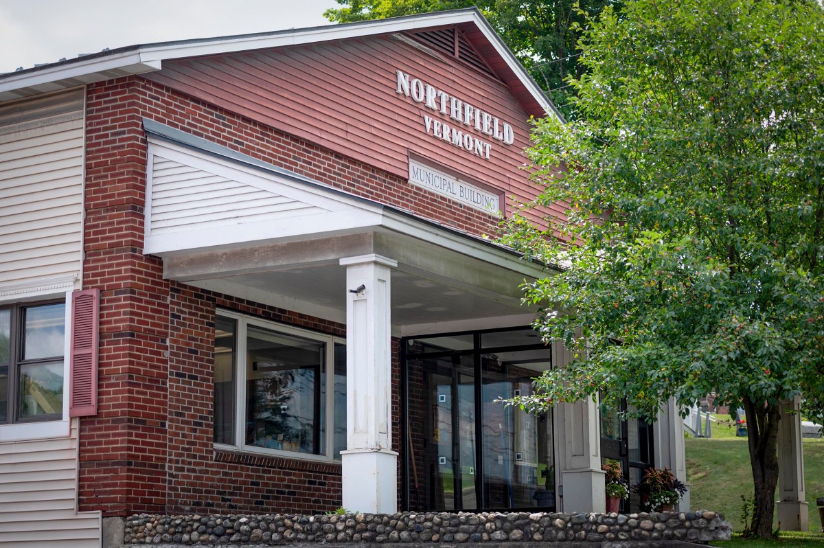 A brick and siding building with a sign reading "Northfield Vermont" above a covered entrance, surrounded by greenery.