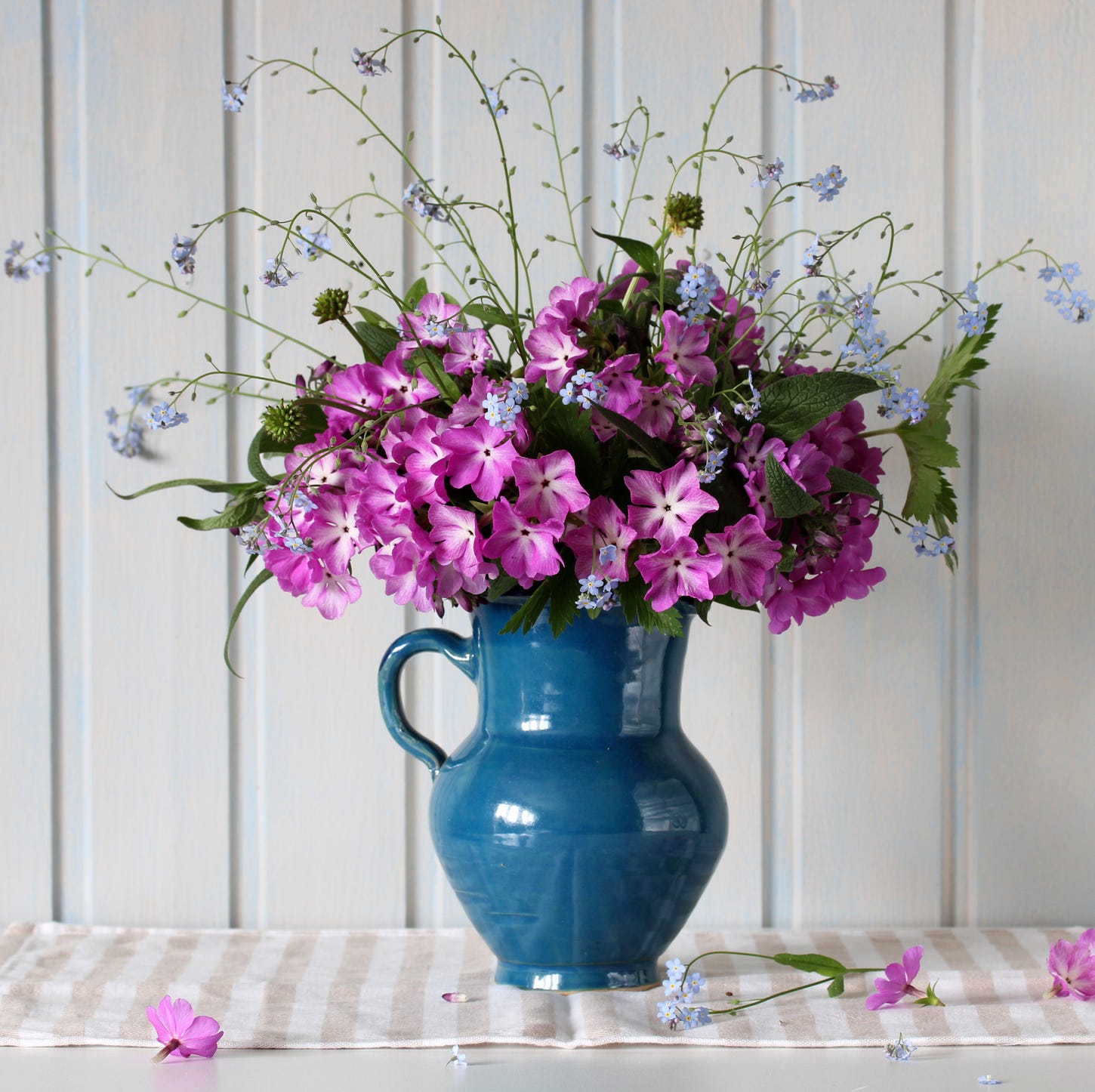 primroses and forget me nots in a jug on the table in a white wooden cottage springtime, rural composition flowers in a vase