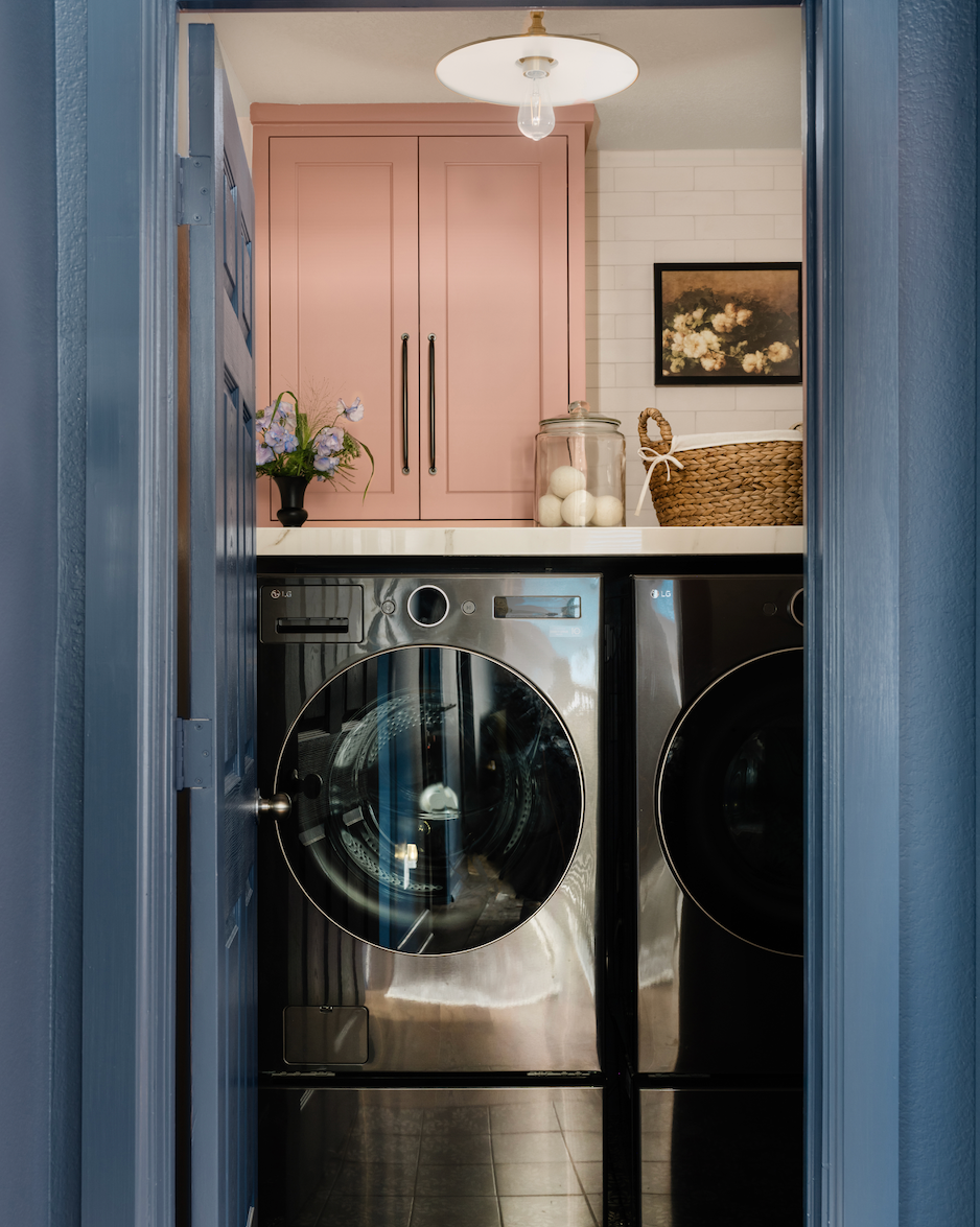 a laundry room with a silver washing machine, a pink cupboard, blue doors, and black and white tiling