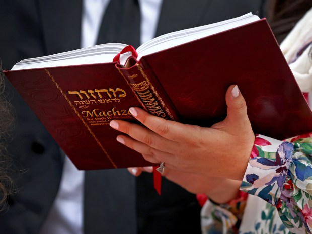 Chenchie Zarchi holds the machzor, a prayer book for the holiday, as her husband Rabbi Mayer Zarchi blows a shofar in the Public Garden on Tuesday. (Nancy Lane/Boston Herald)