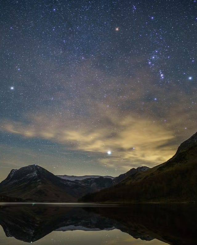 starry night sky over a mountain landscape reflecting in a calm lake
