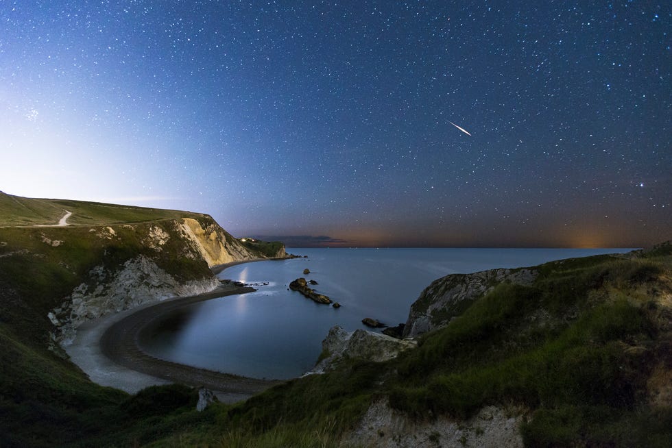 a tranquil night scene on the south coast of dorset. in the picture you can see man o war bay. the picture was taken from the east side of the bay. you can see star and a meteor streaking across the sky.