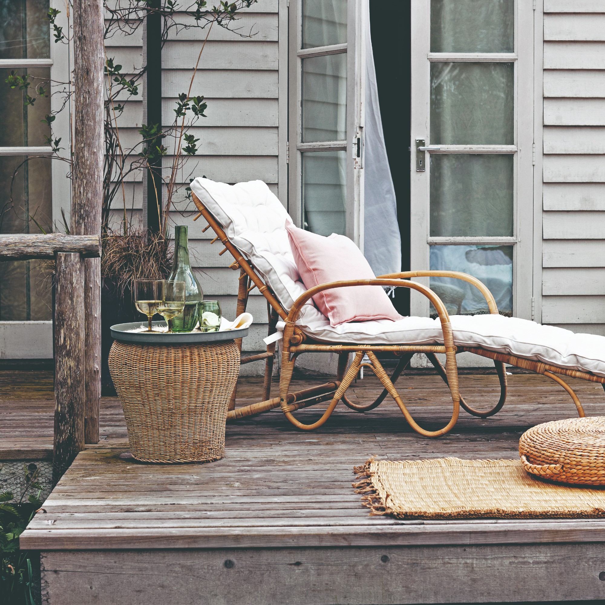 A patio with a rattan sun lounger and side table with a jute rug next to it