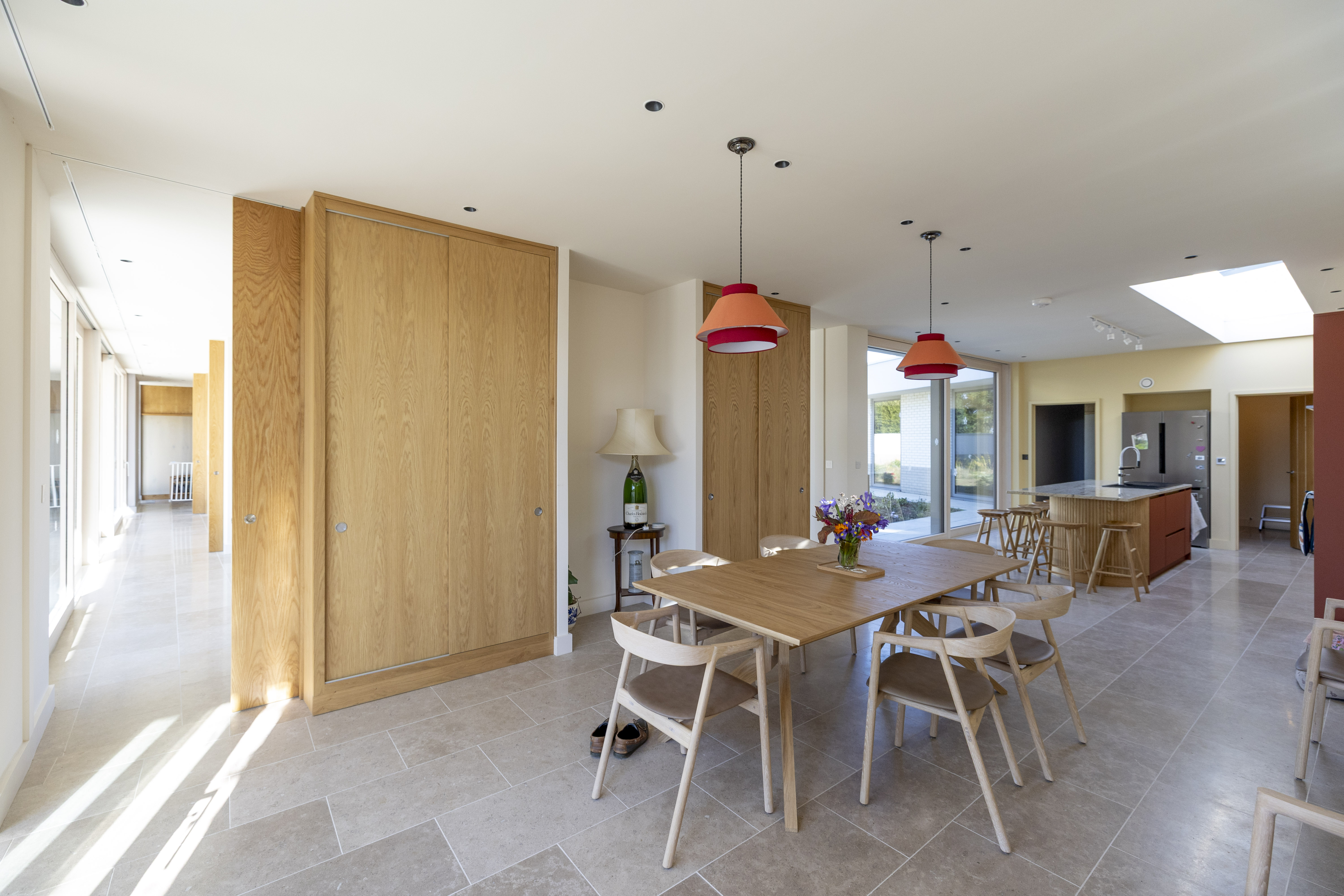 A modernist home with a dining table and chairs in the foreground, a kitchen island in the background, and a hallway to the left.