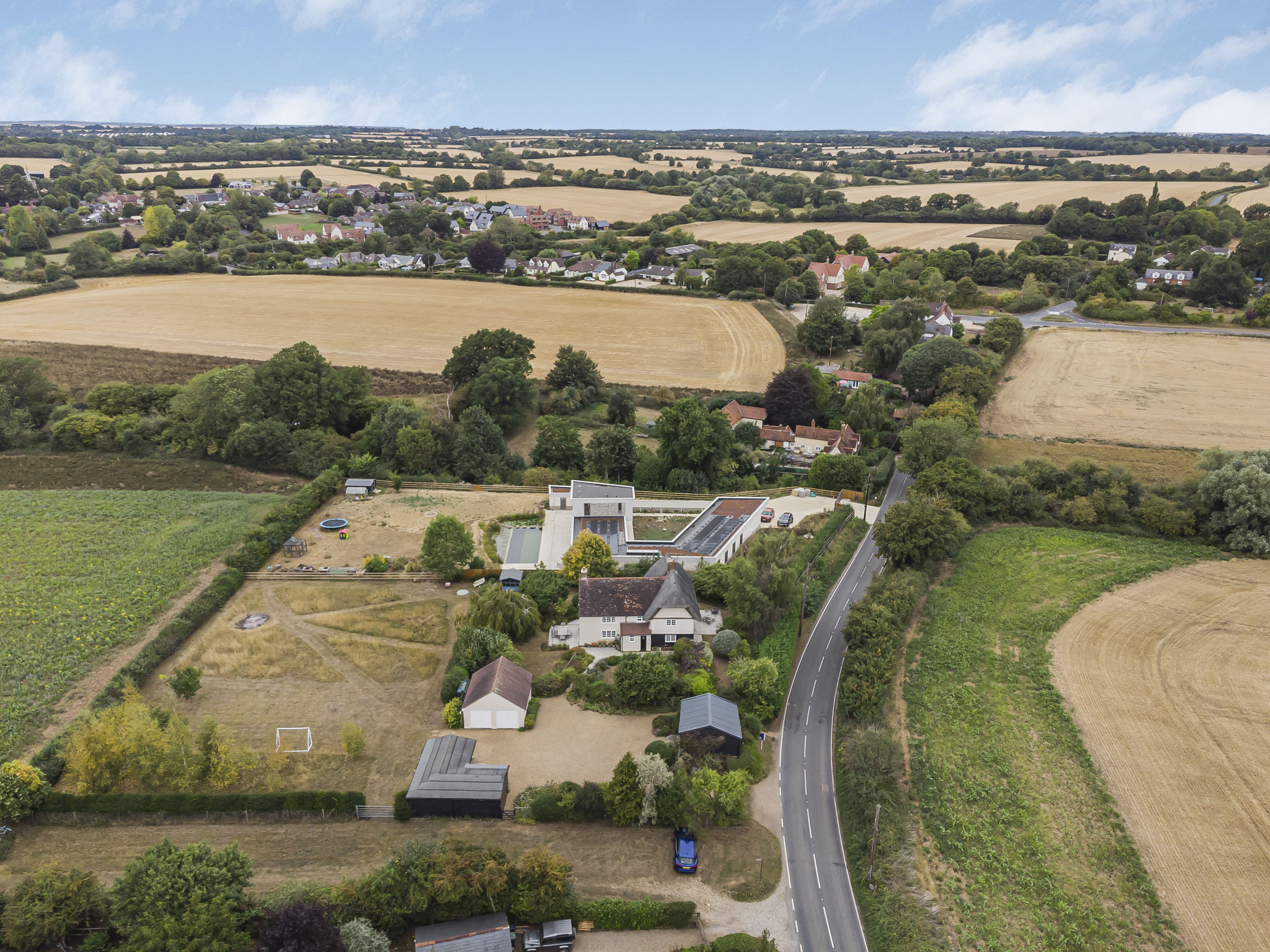 Aerial view of a country house surrounded by fields, trees, and a road.