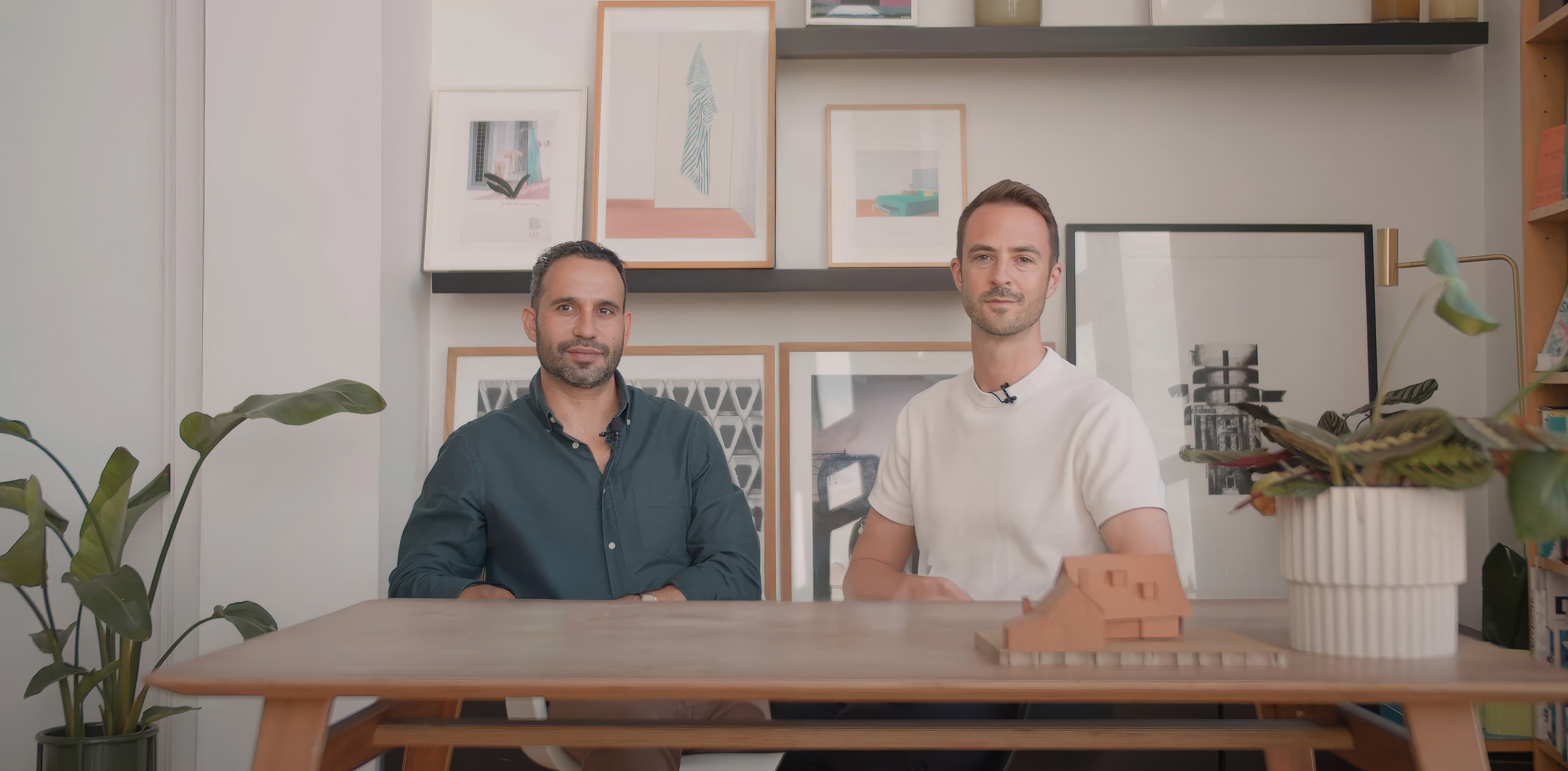 Adam Dainow and Charlie Caswell, founders of Caswell & Daiwnow, sitting at a table with a model house.