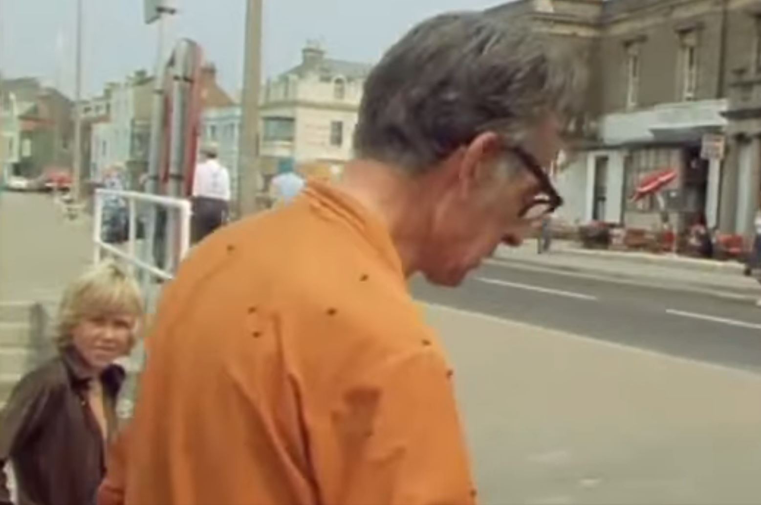 Video still of a man with ladybugs on his orange shirt and a boy next to him.