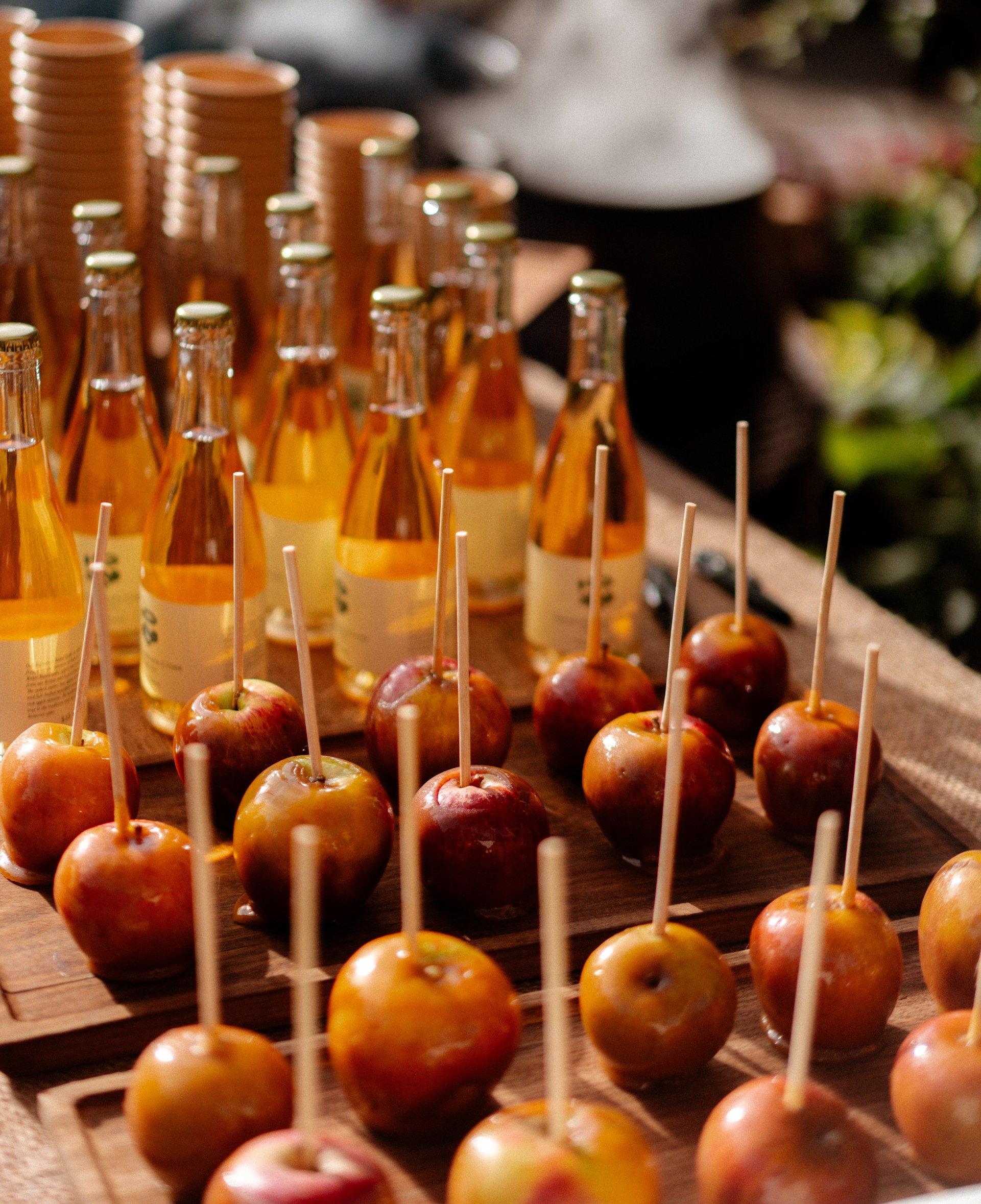 Candy apples and bottled cider on wooden trays.