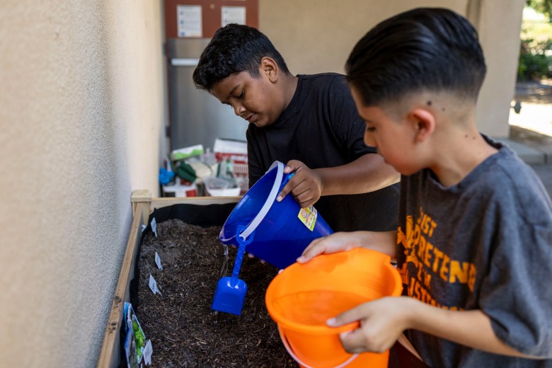 Two children watering a garden bed with buckets.