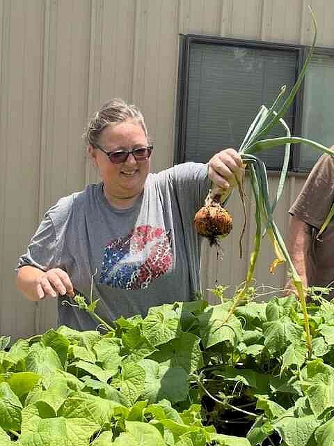 Kristy Hatfield holds an onion over cucumber plants. (Special to The Commercial/University of Arkansas at Pine Bluff)