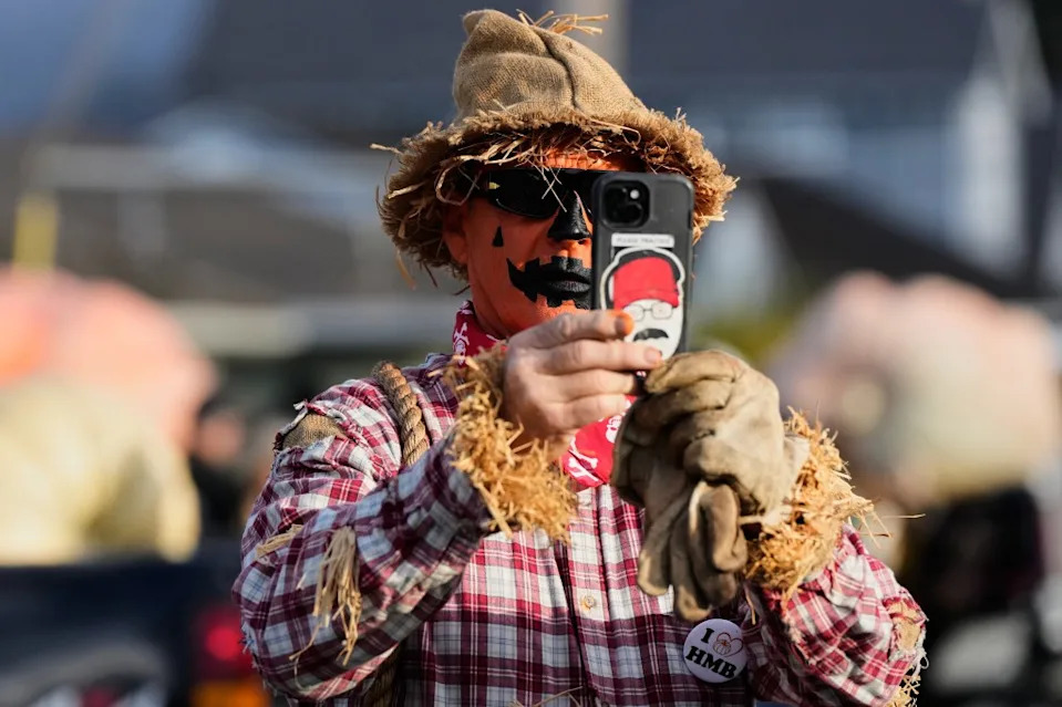 A man dressed as a scarecrow, takes a photo of a giant pumpkin. AP