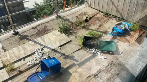 Ian Puckey/BBC A messy balcony with wooden planks as flooring and some indistinguishable rubbish