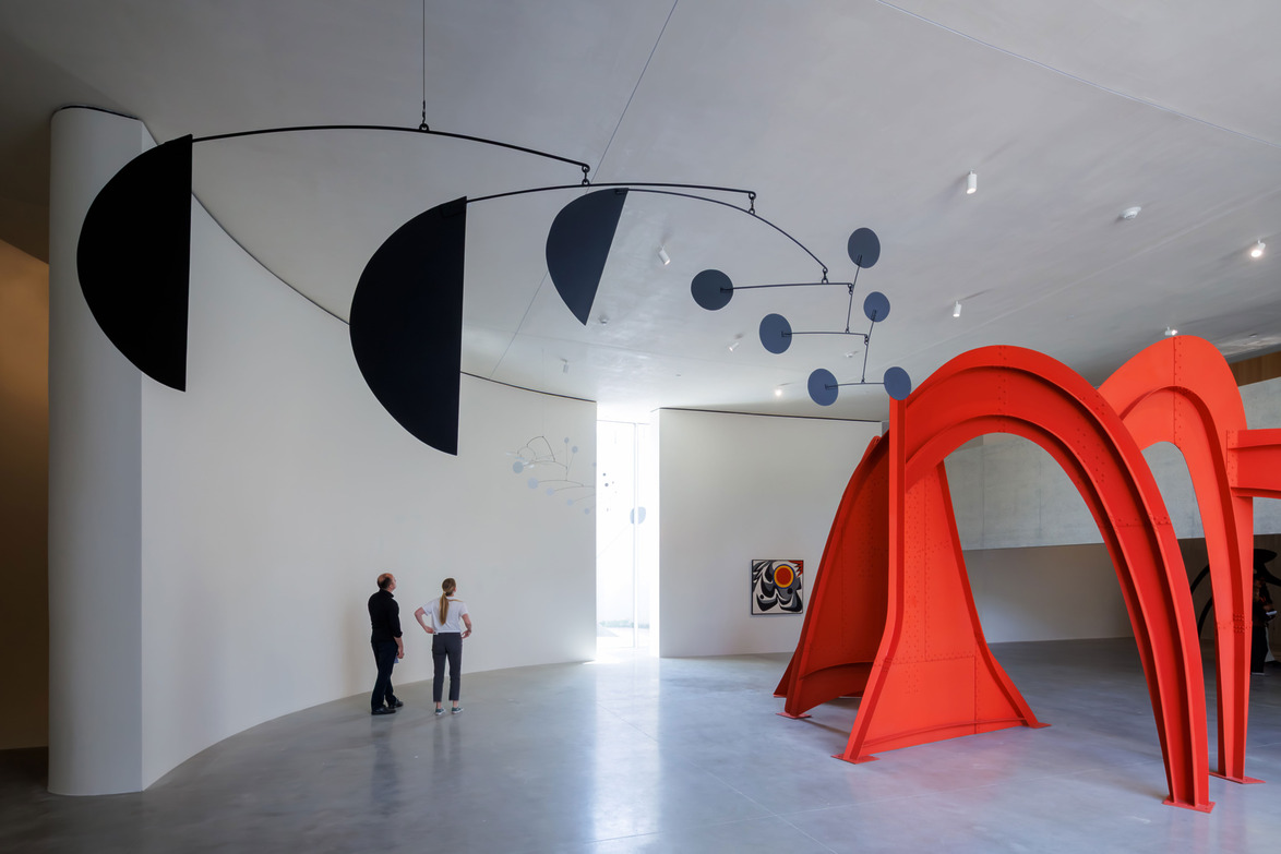Modern art installation featuring a red sculpture and a black mobile hanging from the ceiling in a spacious gallery.