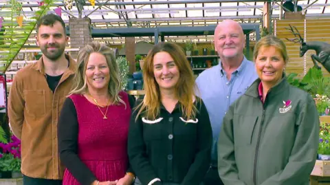 BBC Five adult members of the Stewart family, spanning three generations, posing for the camera in the plant sales area of their garden centre. 