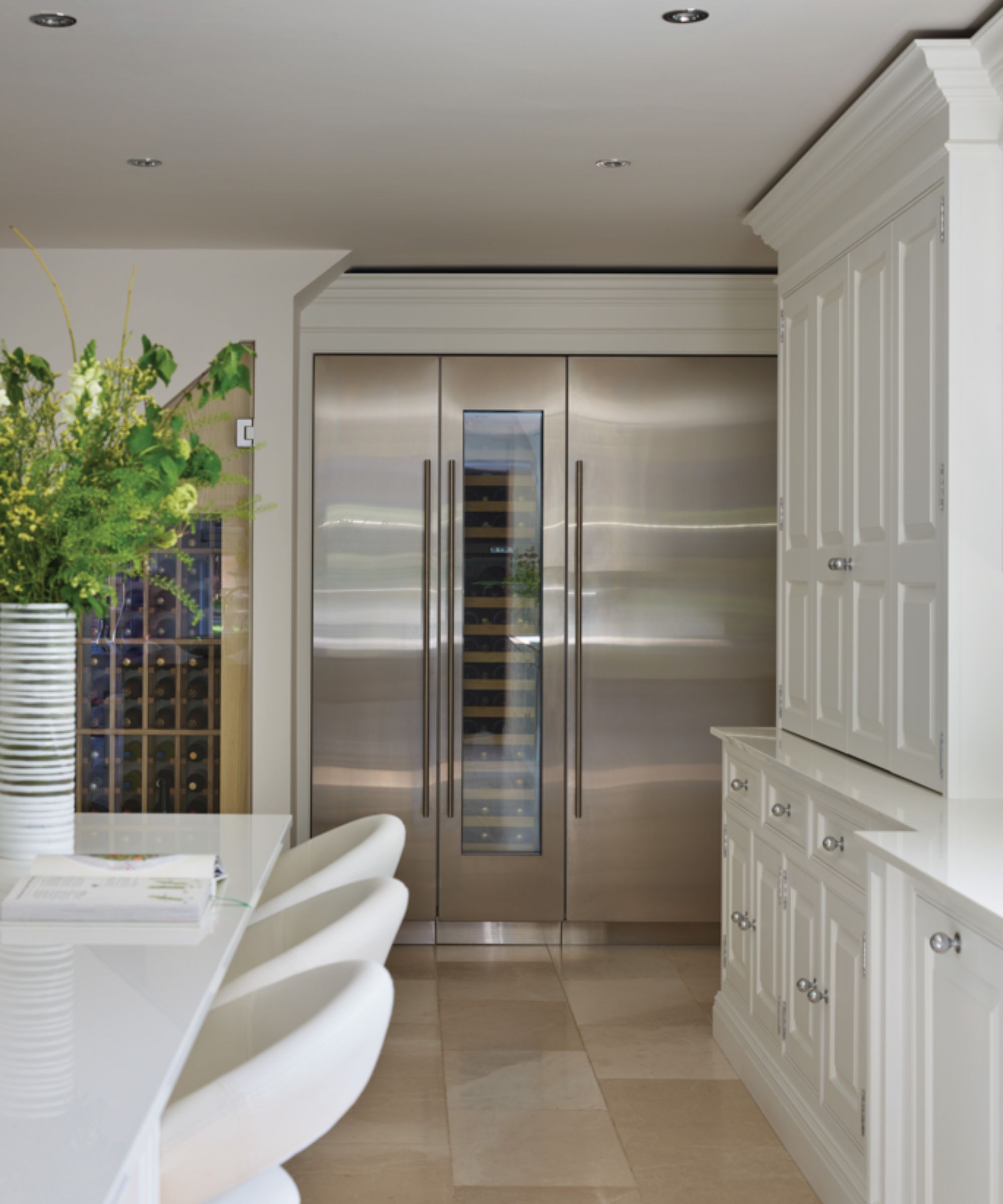Built-in tall silver fridges in a kitchen, one with a wine window showing inside.