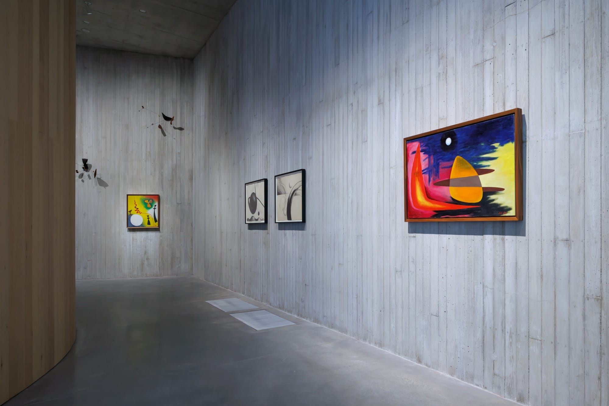 a gray gallery hall at Calder Gardens with works on the wall and two hanging mobiles