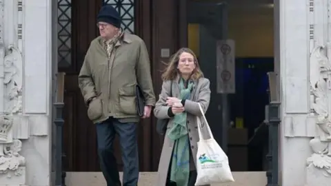 Wales News Service A woman and a man coming down steps outside Newport Crown Court. The man, on the left, wears dark blue trousers and a khaki coat, and a dark blue woolly hat. The woman, on the righ, wears a grey coat and green patterned scarf; she carries a tote bag. 