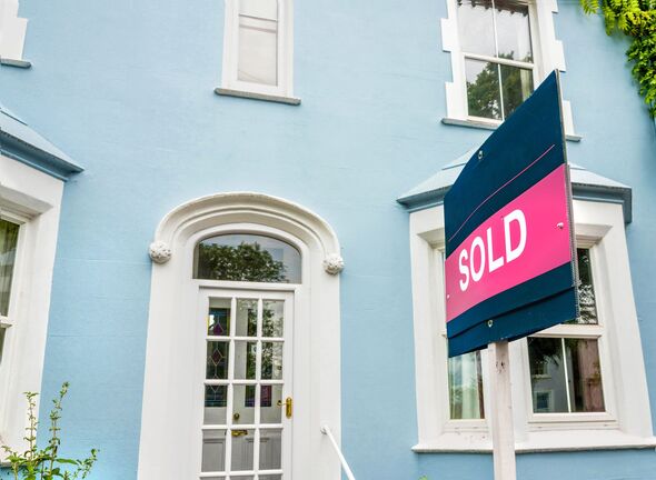 Real estate sign of sold property in front of a beautiful blue house. Sold sign